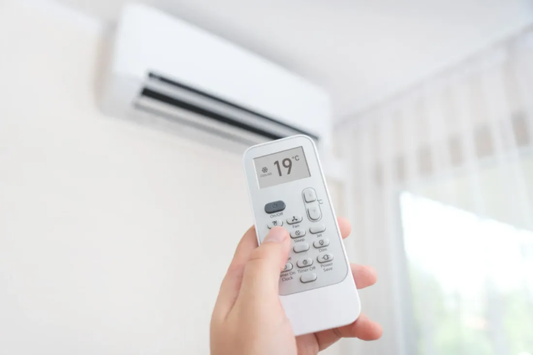 Dłoń kieruje pilot z temperaturą 19 stopni w stronę klimatyzatora ściennego w jasnym pokoju