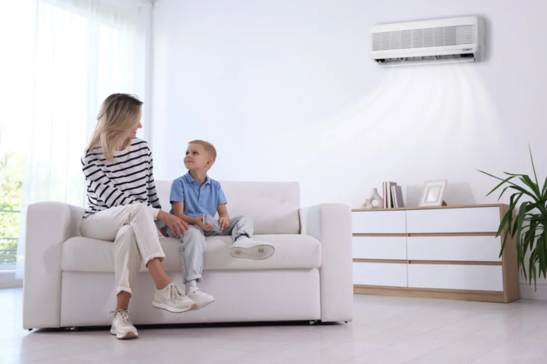 Mama z synem na białej sofie w jasnym salonie chłodzonym przez klimatyzator na ścianie