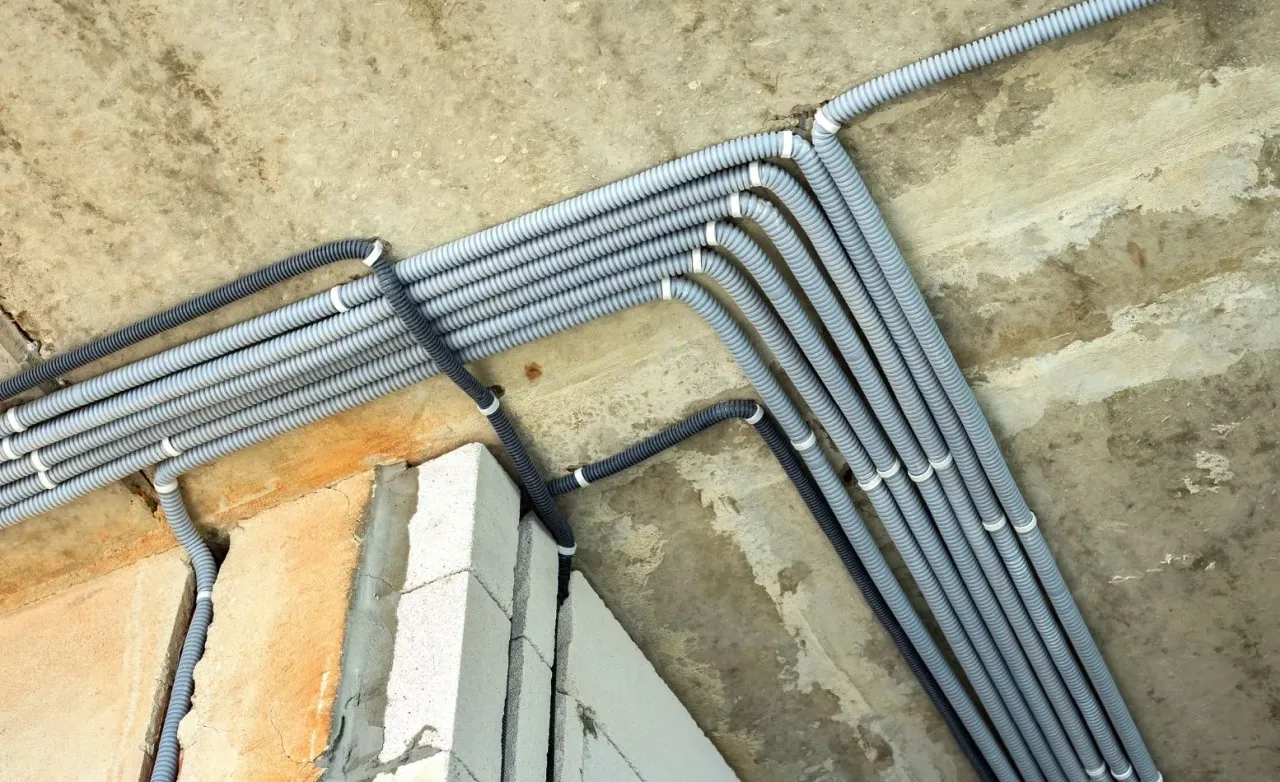 Wiązka szarych peszli elektrycznych poprowadzona pod betonowym stropem nad ścianą z bloczków