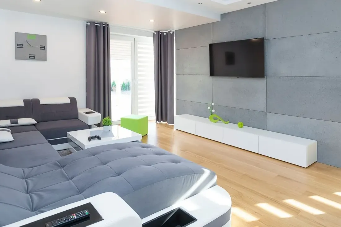 Szary salon z betonową ścianą telewizyjną, dużym narożnikiem i jasną drewnianą podłogą